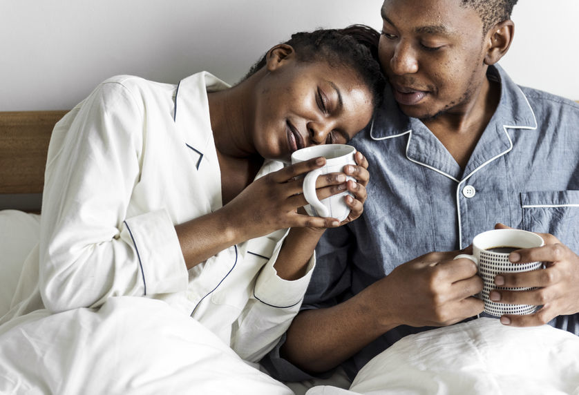 A man and woman sitting in bed, each holding a coffee mug, enjoying a cozy morning together.
