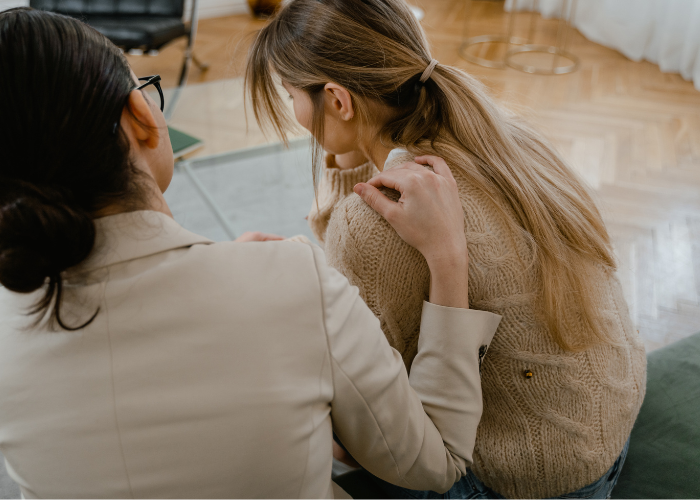 Two women sitting together on a couch in a cozy living room, engaged in conversation