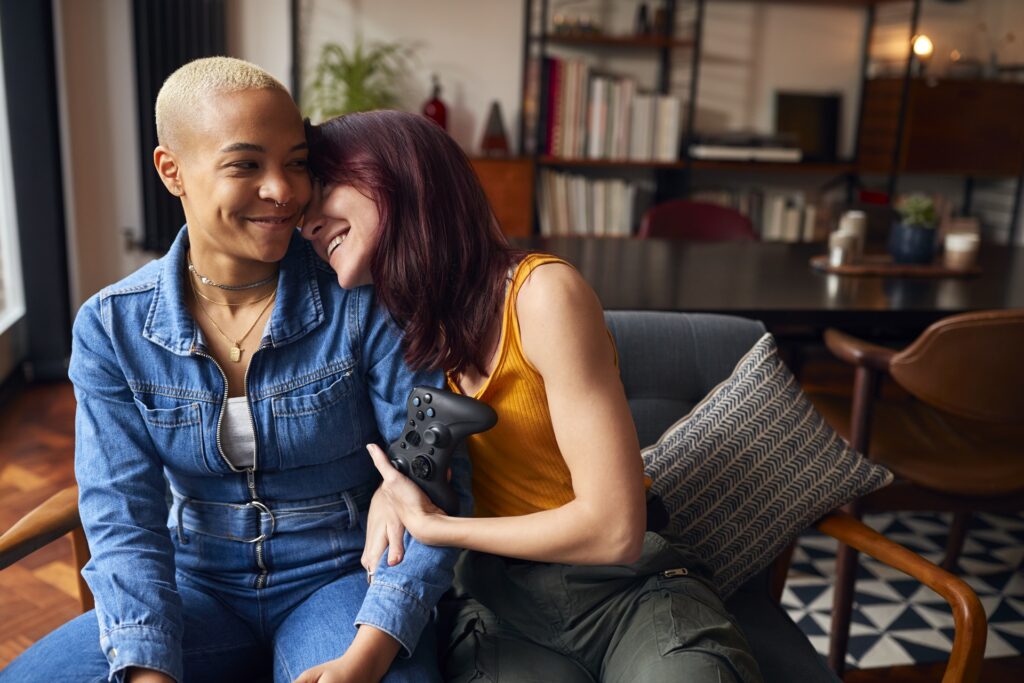 Loving Same Sex Female Couple Sitting On Sofa At Home Gaming Together